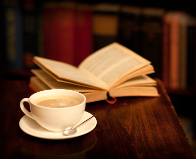 na stole leży otwarta książka, przed nią filiżanka z kawą