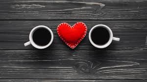 Opis zdjęcia: na ciemnych deskach, patrząc z góry dwie białe filiżanki z kawą, pomiędzy nimi czerwone uszyte ręcznie serce.