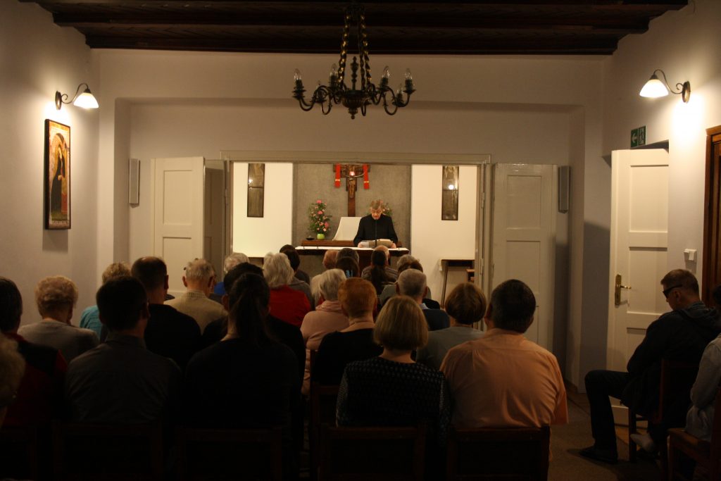Kaplica w domu rekolekcyjnym w Laskach, od tyłu sylwetki siedzących ludzi przodem do słuchaczy przy ołtarzu  ksiądz.