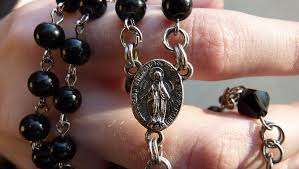 dłoń trzymająca różaniec z medalionem Matki Bożej
