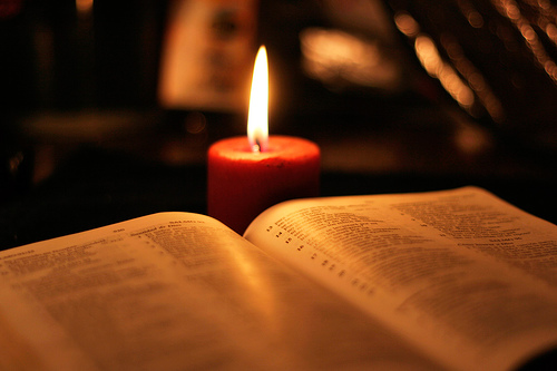 Otarta księga Pisma Świętego, za nią płonąca świeca.