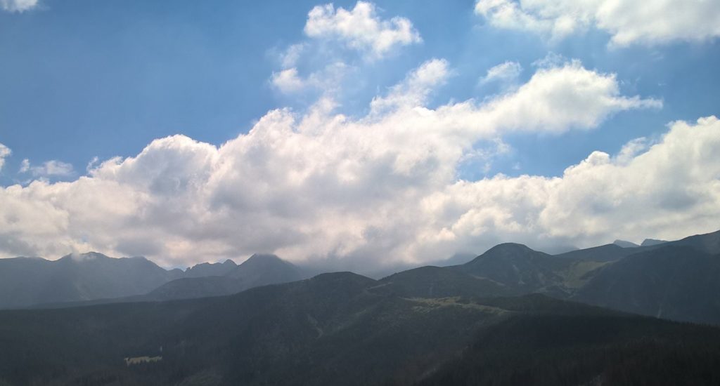 pasmo gór, wyłaniających się z biało-szarych chmur, nad chmurami jasnoniebieskie niebo