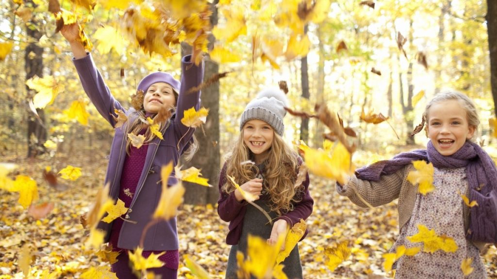 Trzy dziewczynki bawiące się spadającymi liśćmi